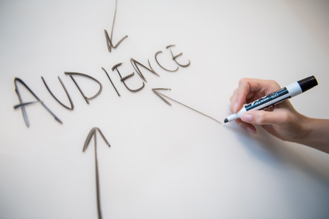 Womans hand writing the word audience on a whiteboard, with arrows.